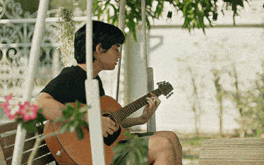 a young man is sitting on a bench playing a guitar