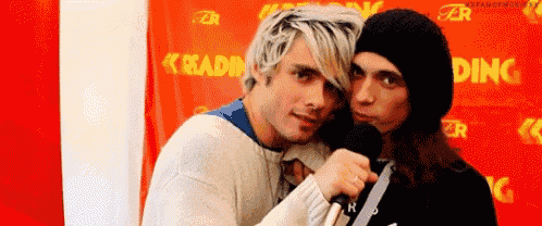two men are hugging each other in front of a red wall with the word reading on it .