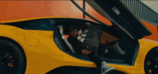 a man sits in a yellow sports car with the hood open