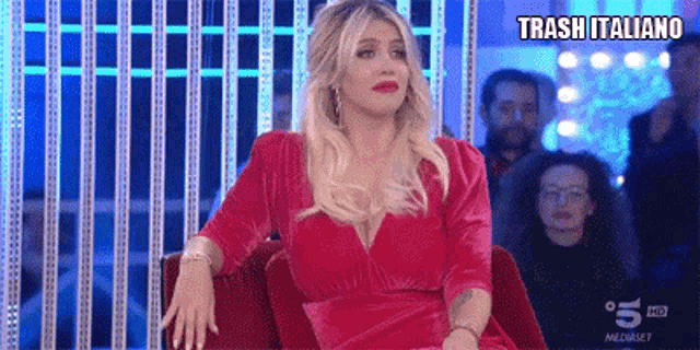 a woman in a red dress is sitting in front of a sign that says trash italiano on it