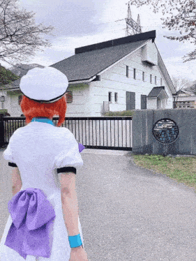 a woman in a white dress with a purple bow on the back is standing in front of a building