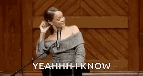 a woman in a gray dress is standing in front of a microphone and saying yeahh i know .