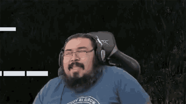 a man with a beard wearing headphones and glasses is sitting in a chair .