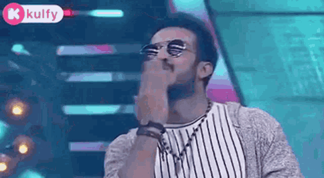 a man wearing sunglasses is covering his face with his hand .