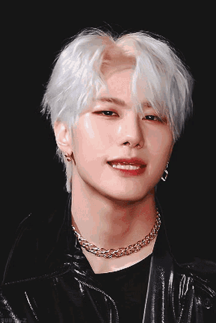 a young man with white hair and a gold chain around his neck is pointing at the camera