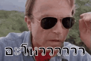a man wearing sunglasses and a blue shirt is making a funny face in a foreign language .