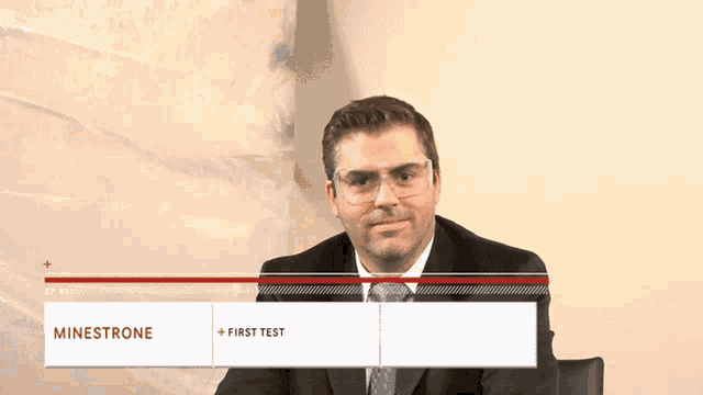 a man in a suit and tie is sitting in front of a sign that says minestrone first test