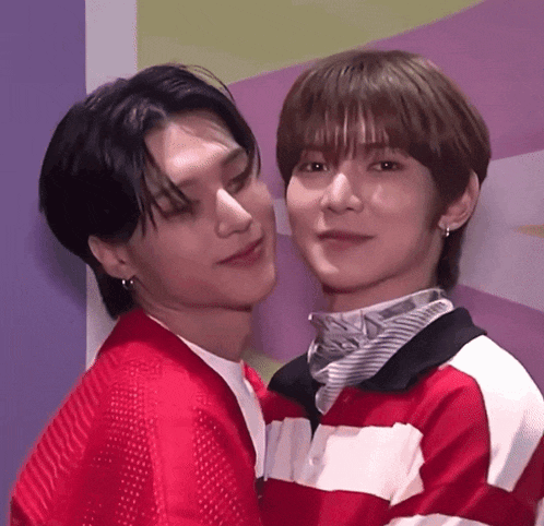 two young men are standing next to each other and one of them is wearing a red sweater .