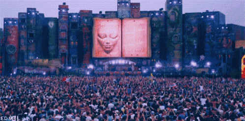 a crowd of people are gathered at a concert with a large screen behind them