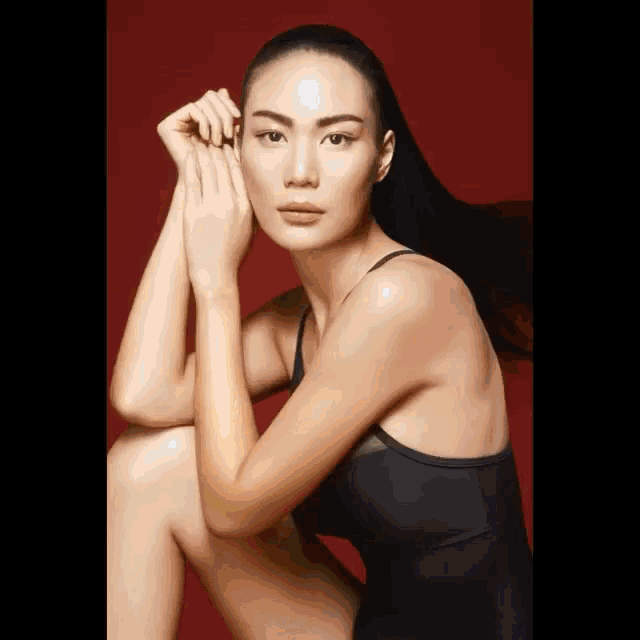 a woman in a black dress is sitting down with her legs crossed and her hands on her face .
