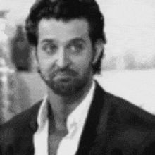 a black and white photo of a man with a beard wearing a suit and a white shirt .