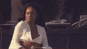 a woman in a white crop top and red bra is sitting on a stage with a record player in the background .