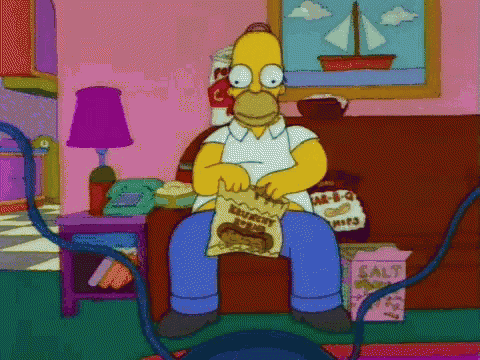 homer simpson is sitting on a couch eating a bag of crunchy chips