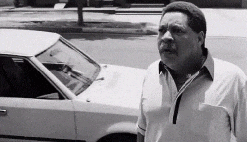 a man is standing in front of a white car on the side of the road .