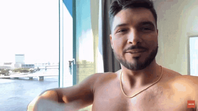 a shirtless man with a gold chain around his neck is smiling and looking at the camera