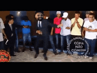 a man in a suit and tie is dancing in front of a group of people with a caption that says copia nao comedia