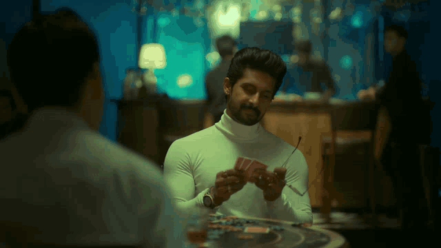 a man in a white turtleneck is holding a pair of cards