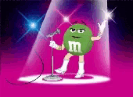 a green m & m is singing into a microphone on a stage