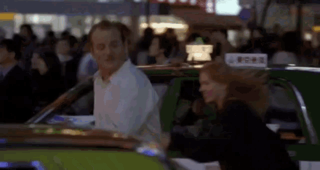 a man in a white shirt is standing next to a woman in a green taxi