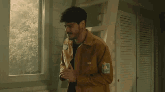 a man in a yellow jacket is standing next to a window .