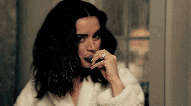 a woman in a white robe is brushing her teeth with a green toothpaste