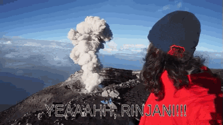 a woman in a red jacket stands in front of a volcano and says yeaaah rinjani