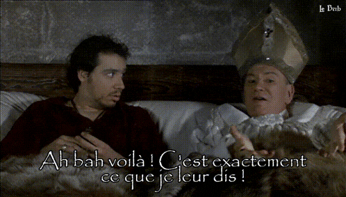 a man in a red shirt is talking to a man in a white robe who is wearing a gold hat