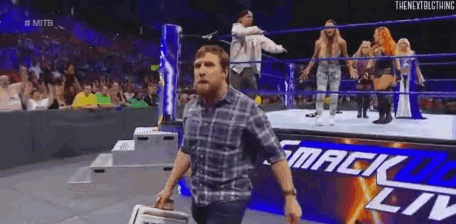 a man in a plaid shirt is walking out of a wrestling ring with a briefcase .