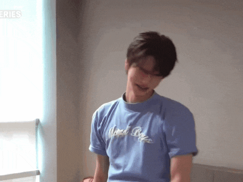 a young man wearing a blue t-shirt is standing in front of a window in a room .