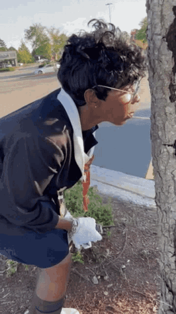 a woman in a black jacket and white gloves is looking at a tree