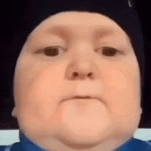 a close up of a baby 's face wearing a hat and making a funny face .