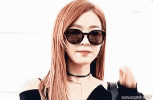 a woman wearing sunglasses and a choker is making a heart shape with her hands .