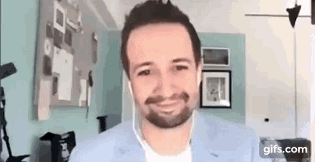 a man with a beard is wearing headphones and smiling while sitting in a living room .