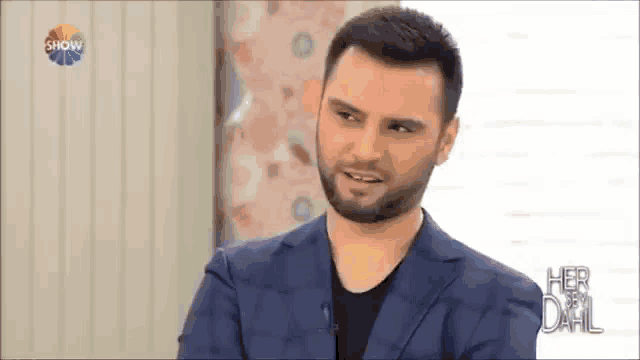 a man with a beard is wearing a blue suit and a black shirt .