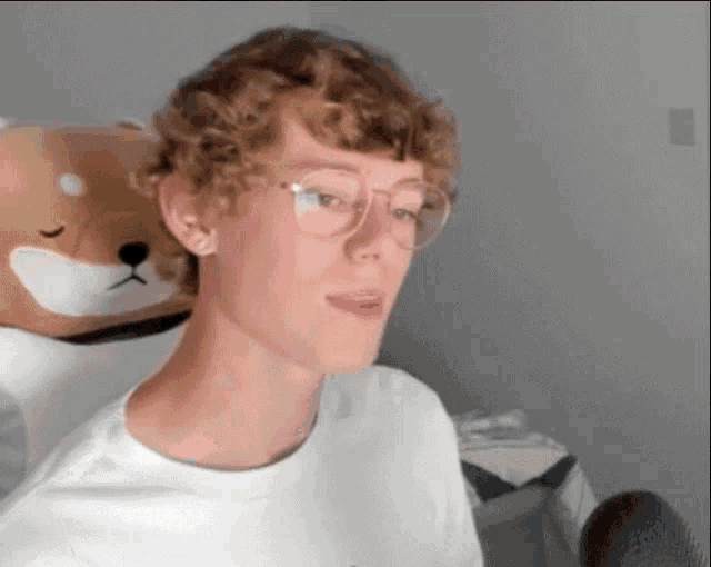 a young man wearing glasses is sitting in front of a stuffed animal .