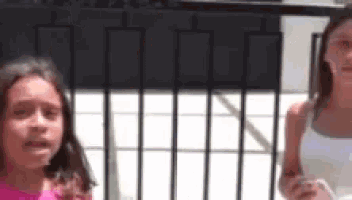 two young girls are standing next to each other on a balcony looking at their phones .