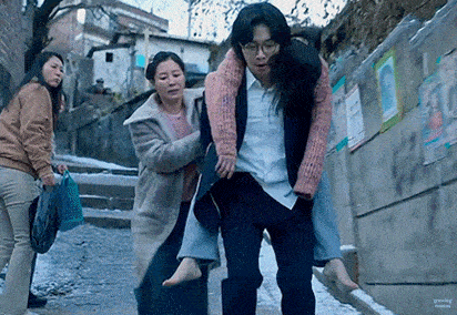 a man is carrying a woman on his shoulders while a woman watches .