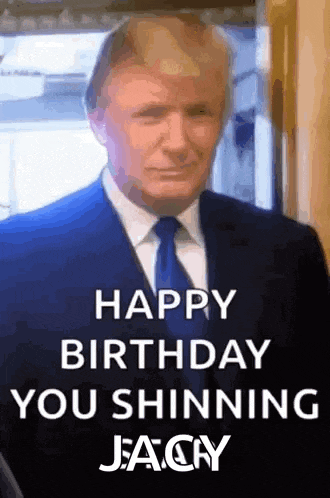 a man in a suit and tie is standing in front of a sign that says `` happy birthday you shining jeacy '' .