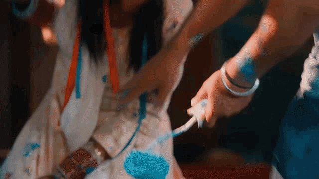 a woman is holding a brush and painting a girl 's shirt blue