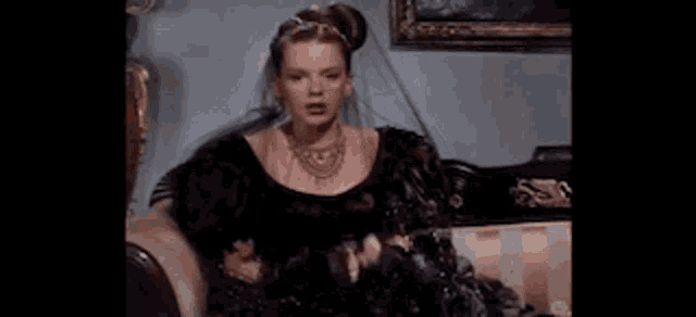 a woman in a black dress is sitting on a couch and making a face .