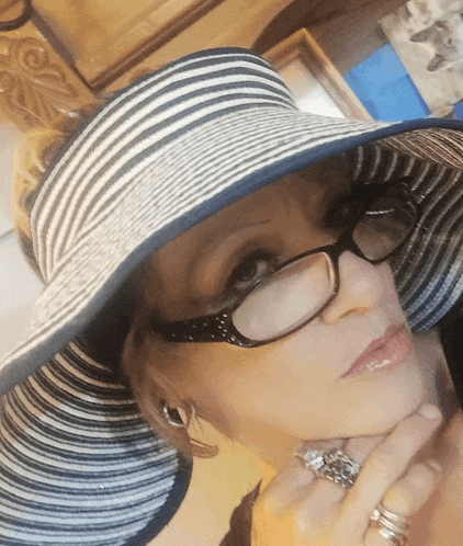 a woman wearing a striped hat and glasses looks at the camera