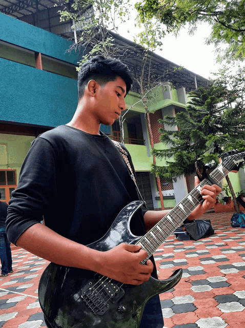 a young man in a black shirt is playing a guitar