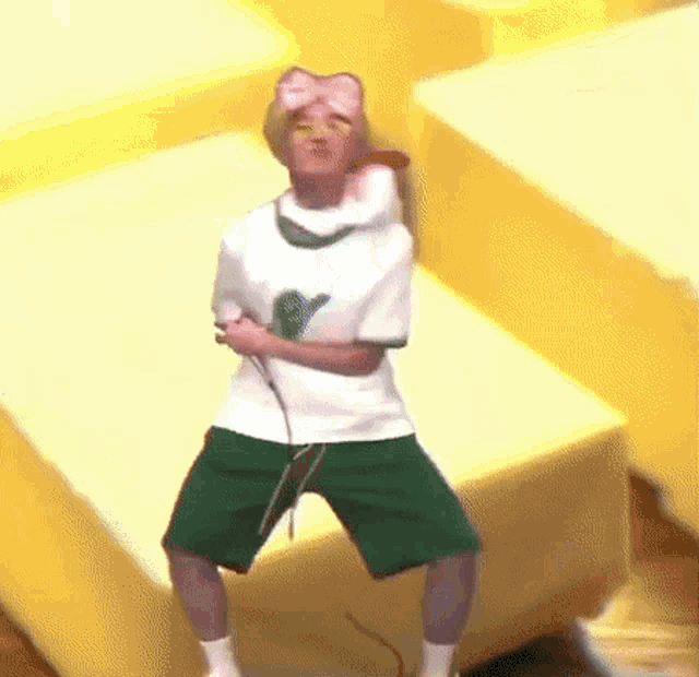 a man in a white shirt and green shorts is holding a microphone and dancing on a set of stairs .