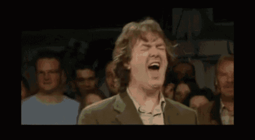 a man in a green jacket is laughing in front of a crowd .