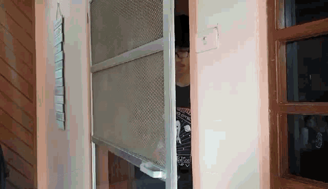 a man is peeking out from behind a screen door in a room .