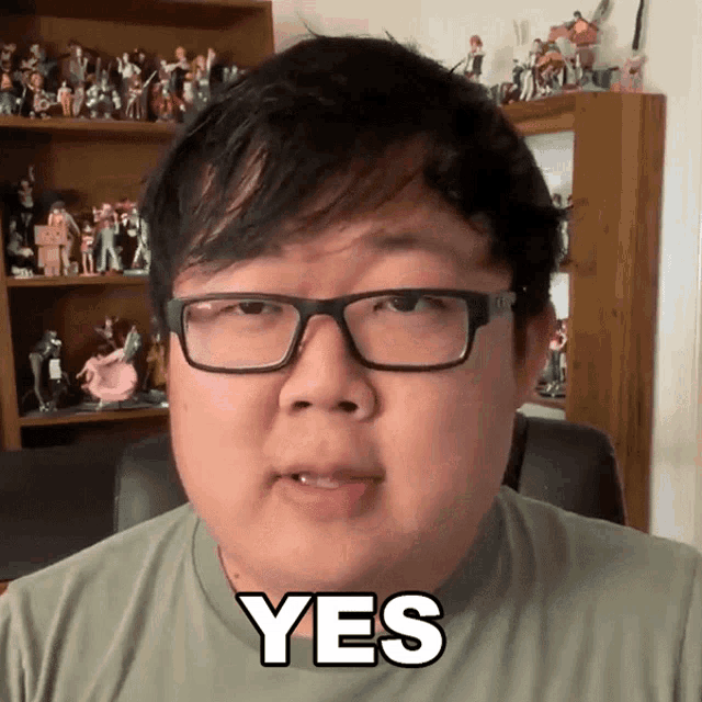 a man with glasses says yes in front of a shelf full of figurines