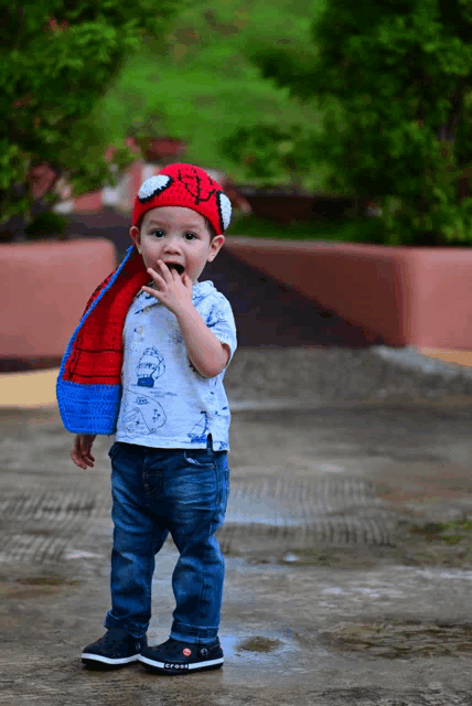 a little boy wearing a spiderman hat and scarf covering his mouth