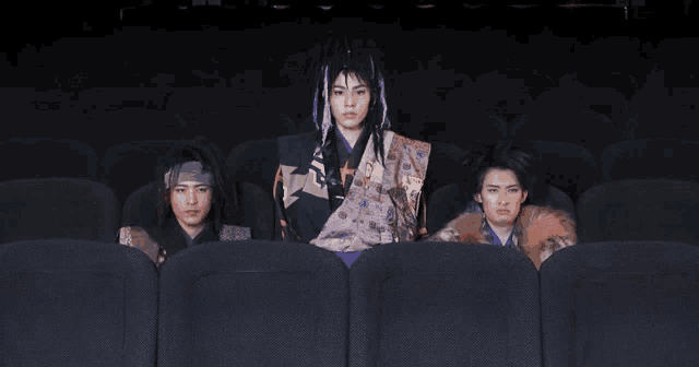 a man in a samurai costume sits in a theater with two other people