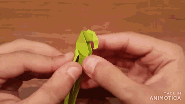 a close up of a person holding a green origami animal with the words made in animotica below it