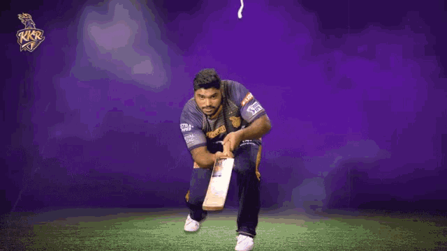a man holding a cricket bat in front of a purple background with the letters rkr on it